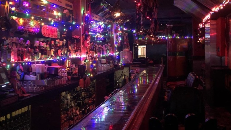 The bar at Kozy Kar lit by colorful string lights, with vintage car decor and shelves of bottles.