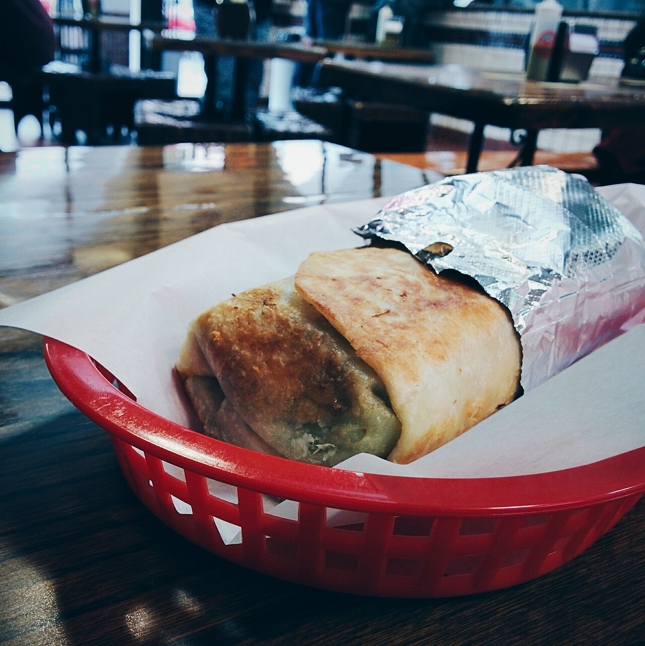 A toasted carnitas burrito served in a red basket at La Taqueria.