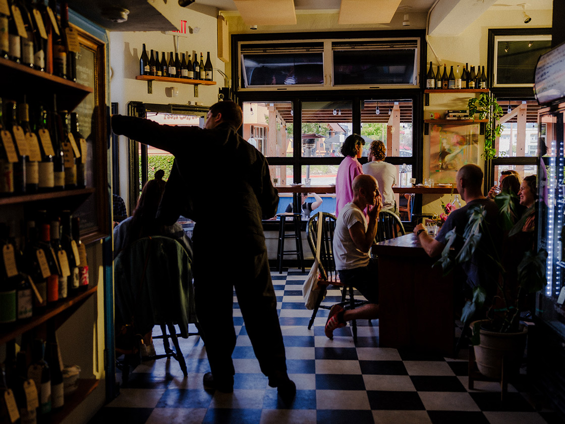 Guests and wine shelves in Snail Bar’s intimate dining room, with its blue-and-white tiled floor.